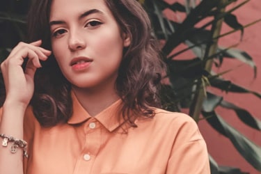 woman modelling maroon shirt against a dark green background, looking forwards at the user